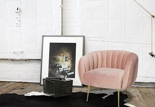 A pink chair and black trunk in front of a white wall.