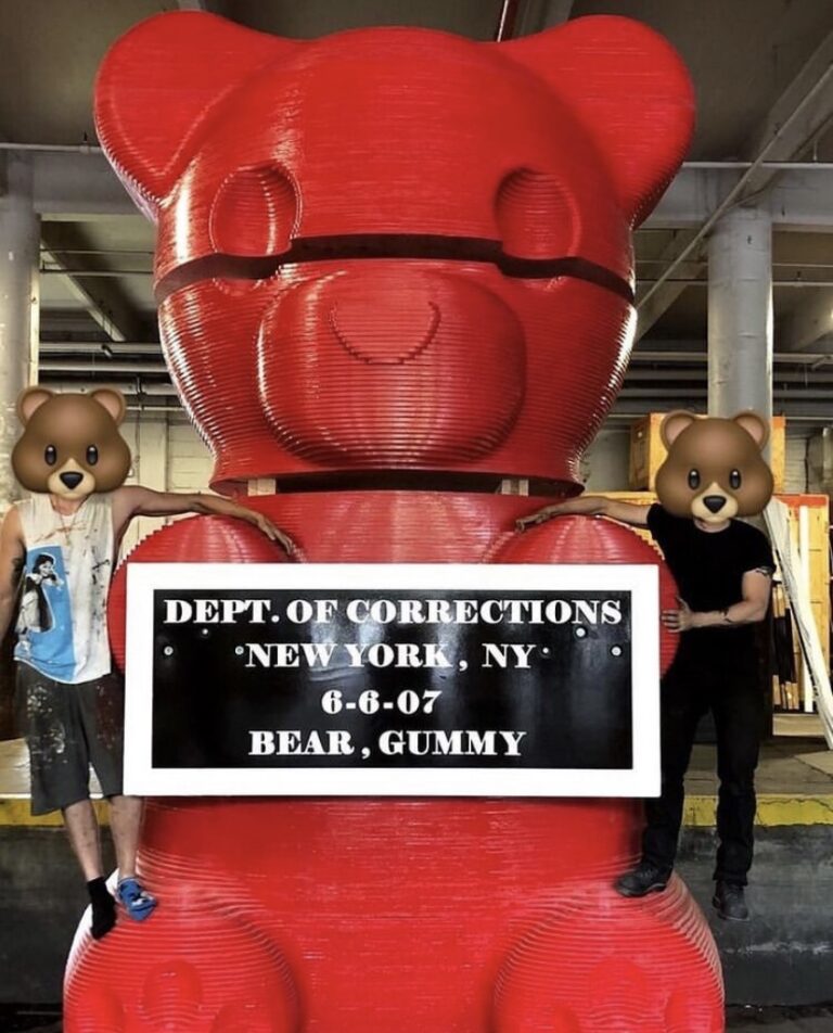 A giant red bear statue with two people standing next to it.